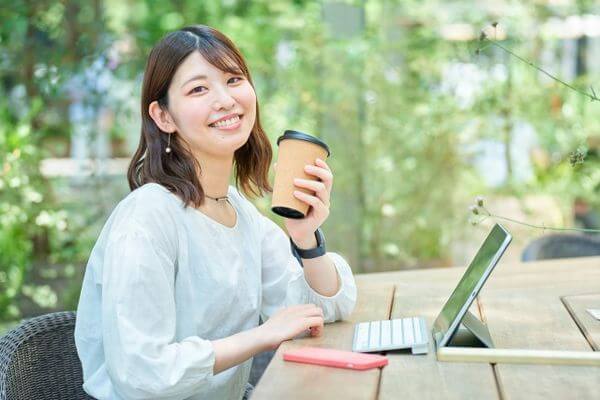 コーヒーを手に街角でPC操作して、ブログを書いている笑顔の女性